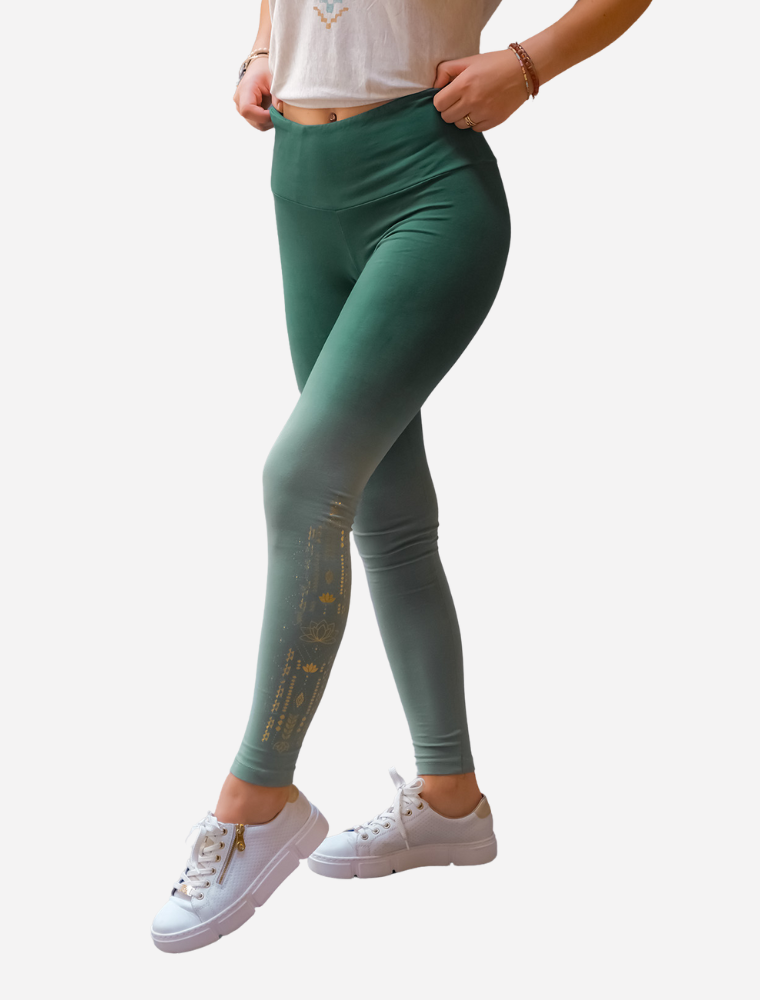 Frau in der Yoga Leggings in smaragdgrün von Spirit of OM mit seitlichem Goldfoliendruck am Bein. Ein zarter Farbverlauf des Stoffes, der von oben nach unten heller wird.