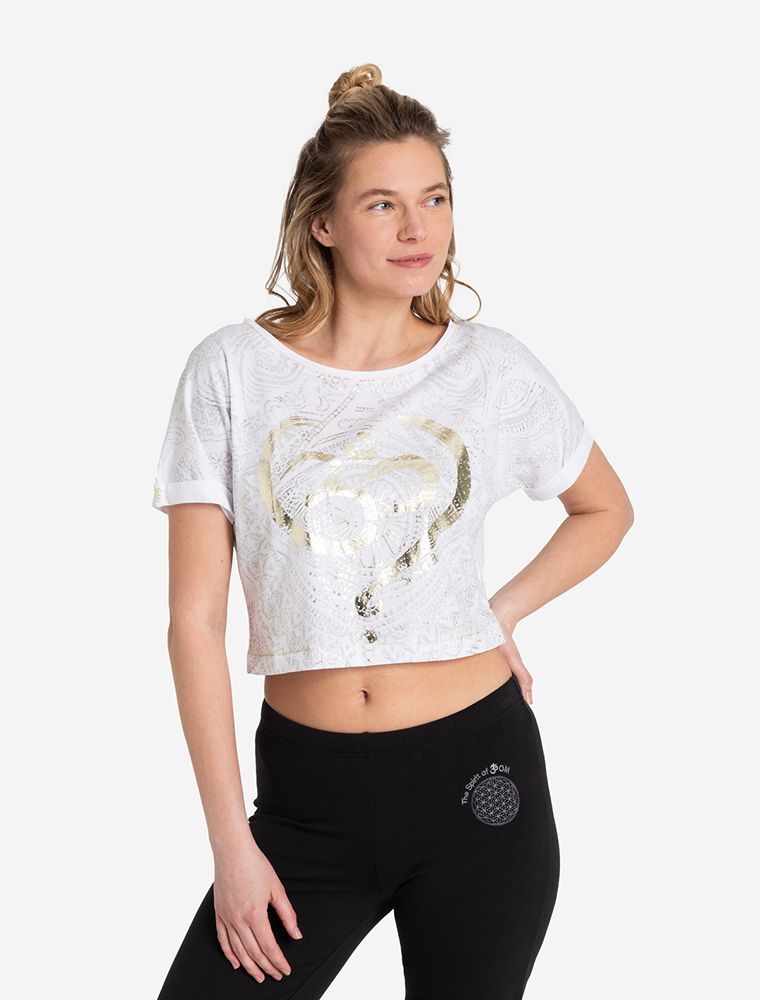 Frau trägt das Coop Shirt OM Time von  Spirit of OM. Weißes Shirt mit einem OM in Goldfolie und silbernen Mandalas. Bauchfrei. Schwarze Yogahose mit weißer Blume des Lebens 