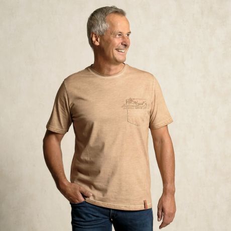 Fröhlicher Mann mit Blick zur Seite. Er trägt das Bio-Baumwoll Shirt in zirbenbraun. Eine helle, erdige Farbe mit Flamm-Effekt und stilisierter Druck eines Berges auf der Brusttasche.