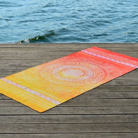 Beach towel in warm colors of yellow and orange laid out on a wooden jetty. Next to it you can see directly the water, which is moved in small waves by the wind.